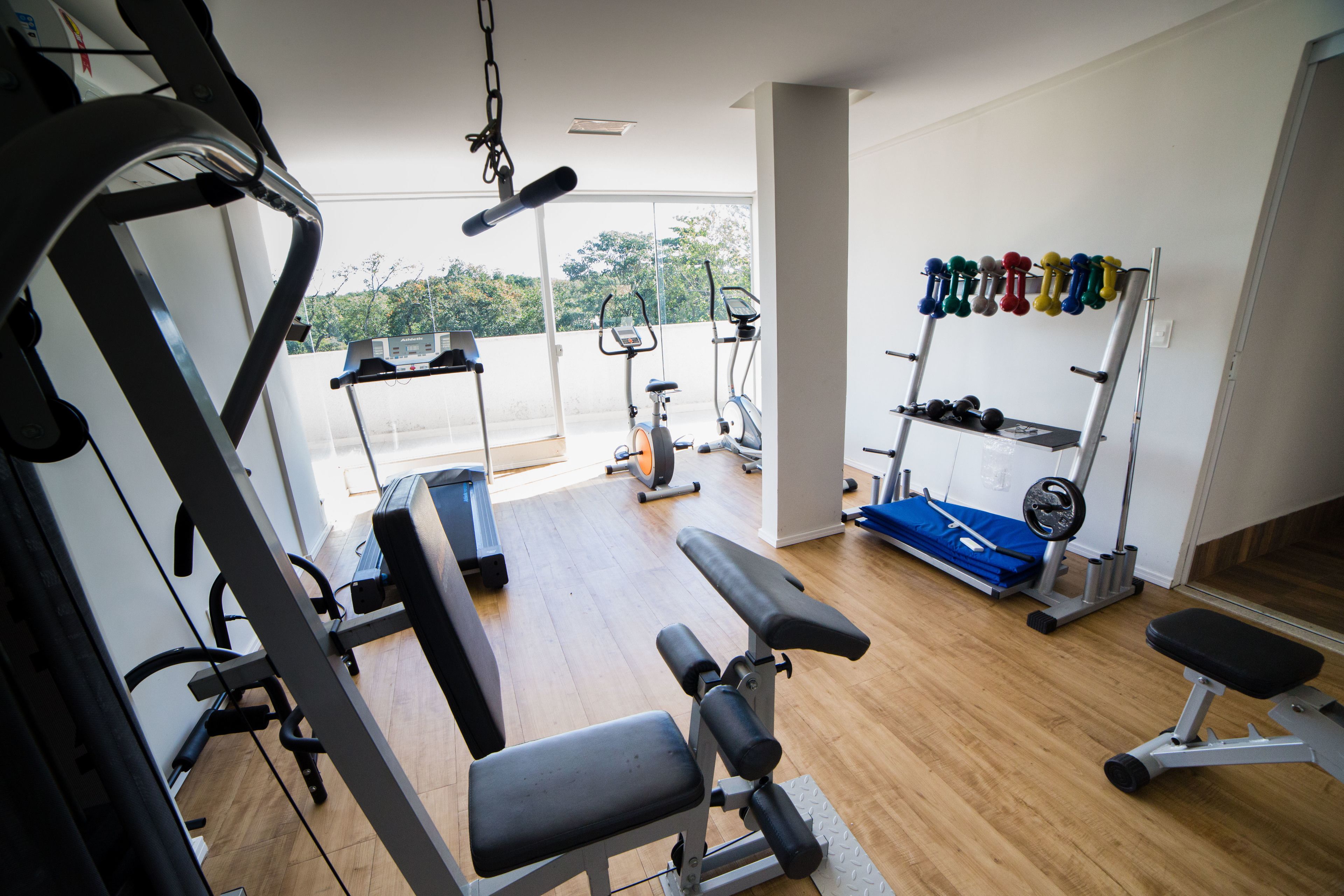 A gym with exercise equipment, a bench, and a rack of dumbbells.