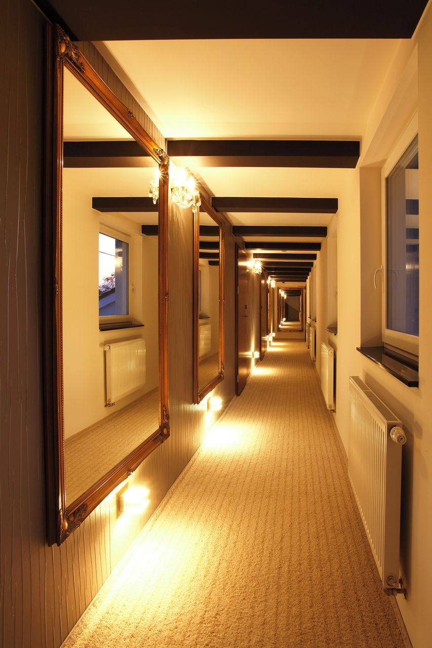 Un couloir d’hôtel avec un plancher en bois, des murs recouverts de miroirs et un radiateur sur le côté droit.