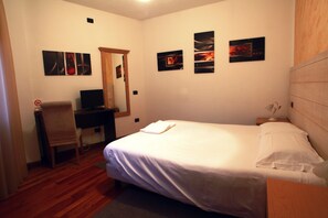 A bedroom with a bed, a desk, a chair, and artwork on the walls. - De La Tour (Tirano)