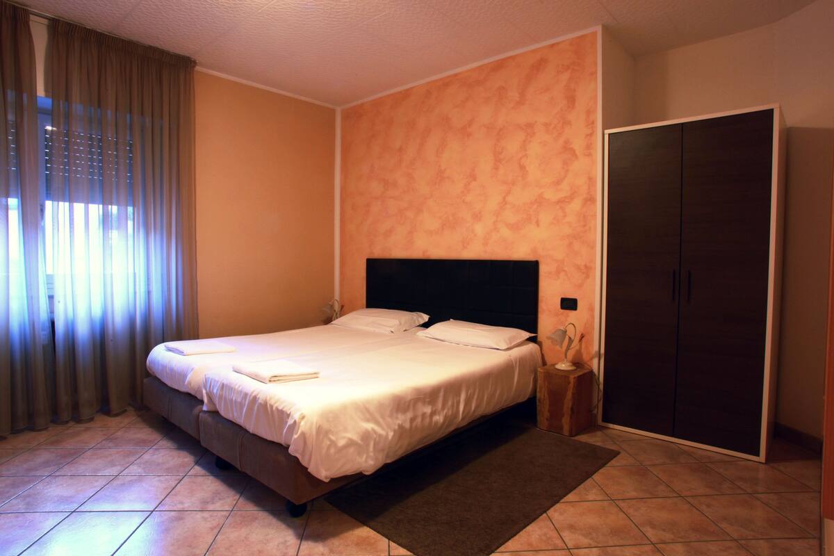 A neatly made bed with white linens, a dark headboard, and a wooden nightstand with a lamp.