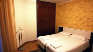 A hotel room with two beds, a wooden wardrobe, and a coat rack. - De La Tour (Tirano)