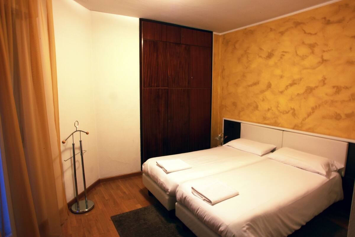 A hotel room with two beds, a wooden wardrobe, and a coat rack.