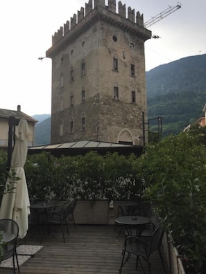 A stone tower with arched windows, surrounded by greenery and wooden deck with outdoor seating. - De La Tour (Tirano)