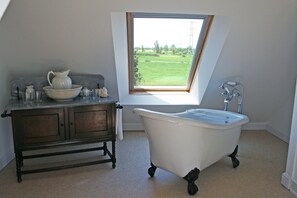 Un baño con una bañera independiente, un tocador de madera con lavabo y una ventana con vistas a un campo verde.