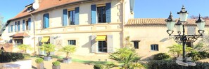 Un bâtiment doté de nombreuses fenêtres, dont certaines sont équipées de volets, d’un auvent jaune et d’une enseigne indiquant « Toilettes ».