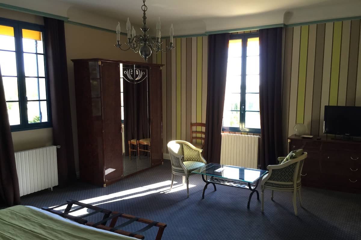 A hotel room with a bed, a desk, a chair, a wardrobe, a television, and a chandelier.