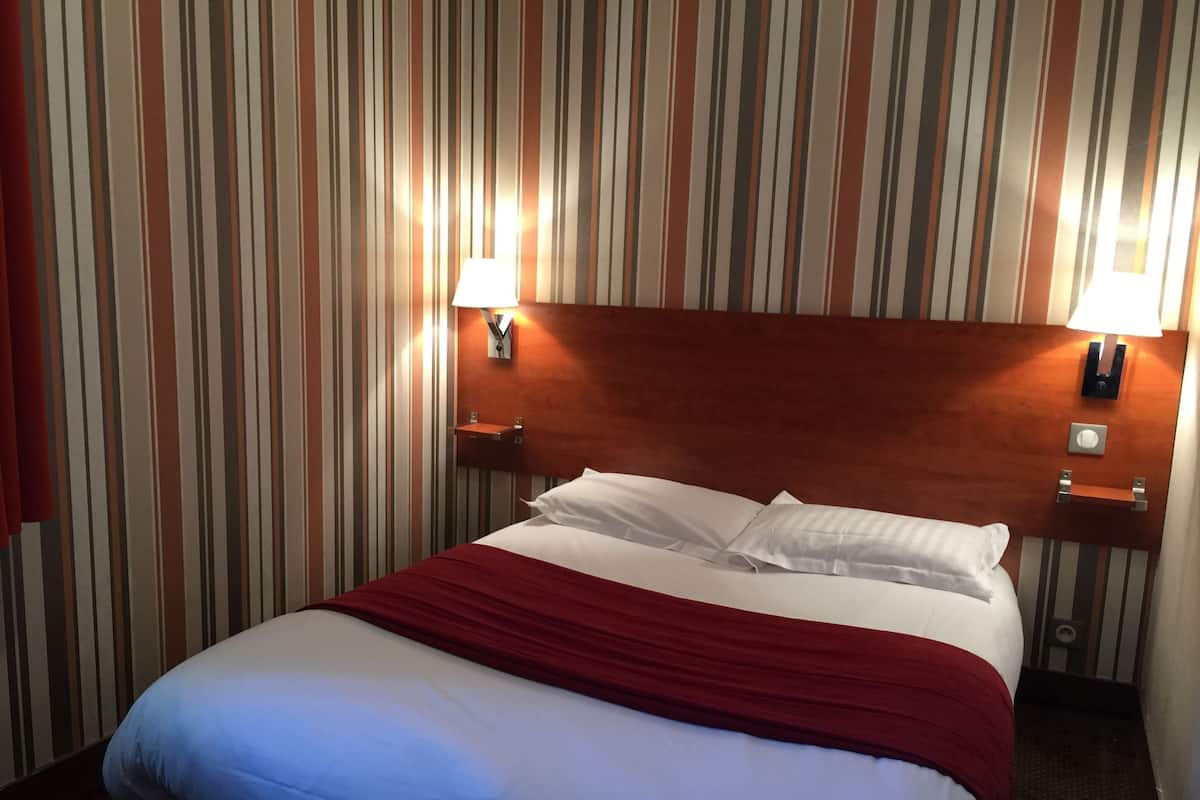 A hotel room with a bed, striped wallpaper, and two bedside lamps.