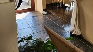 Un corridoio d'albergo con pavimento piastrellato, una sala da pranzo con tavolo e sedie e un elemento decorativo appeso al muro.