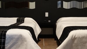 Una camera d'albergo con due letti, un comodino e una lampada fissata al muro.