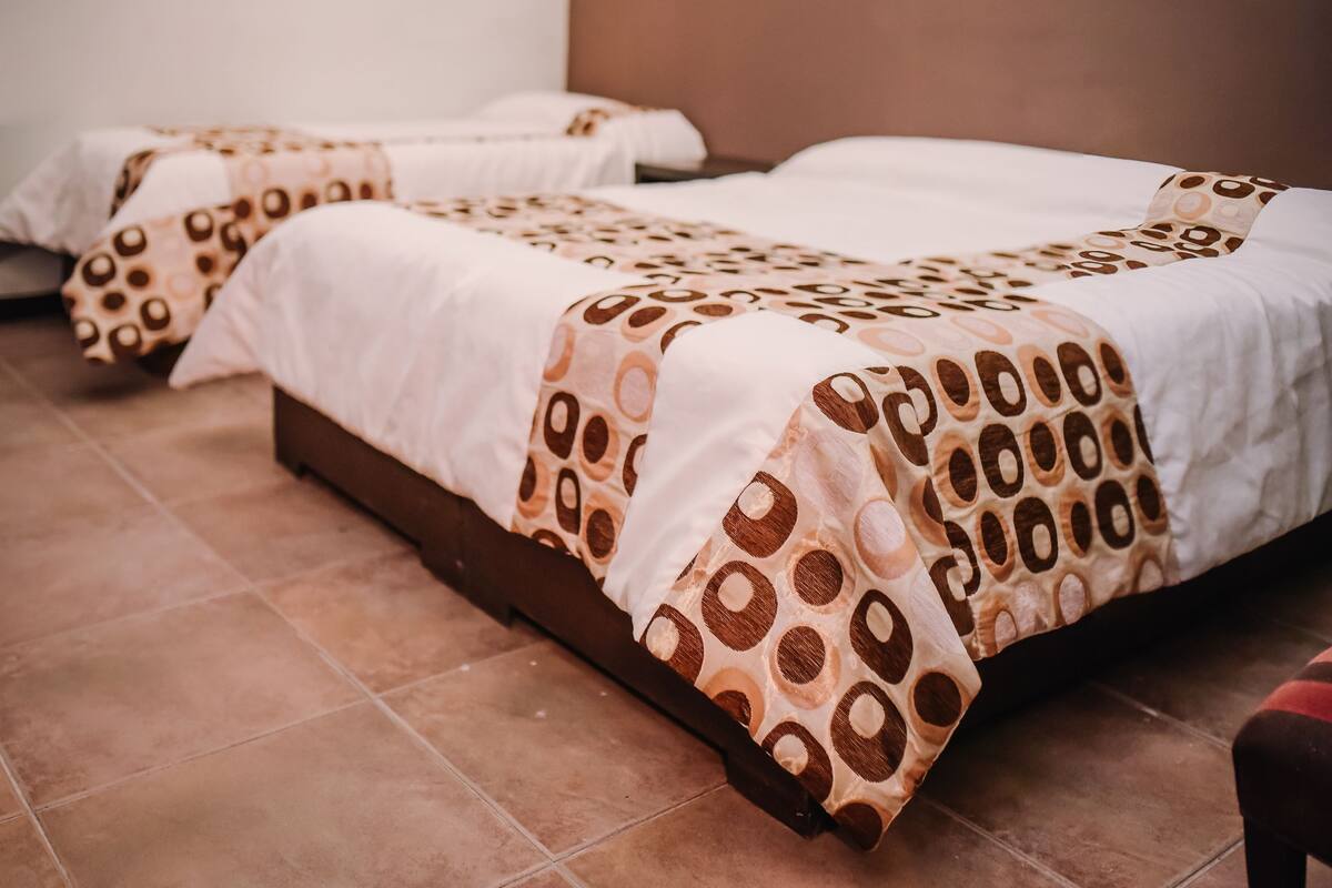 A hotel room with two beds, each with a patterned bedspread and a wooden headboard.