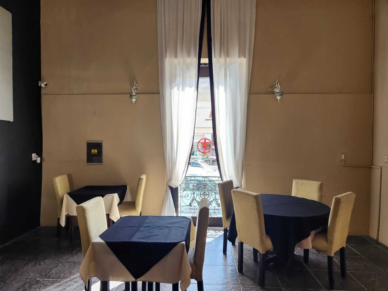 A dining area with tables and chairs, a view of the street through a window, and a door on the left.