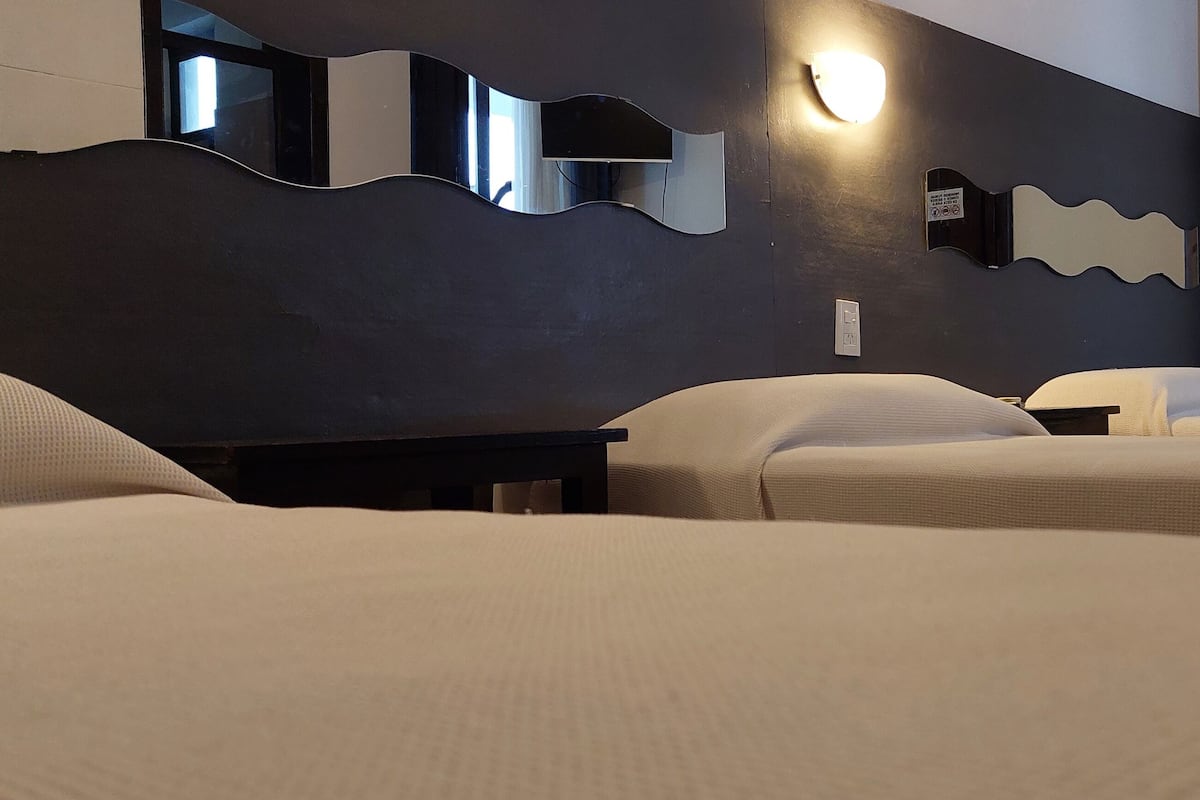 A hotel room with two beds, a dark wall, and a mirror with a wavy design.