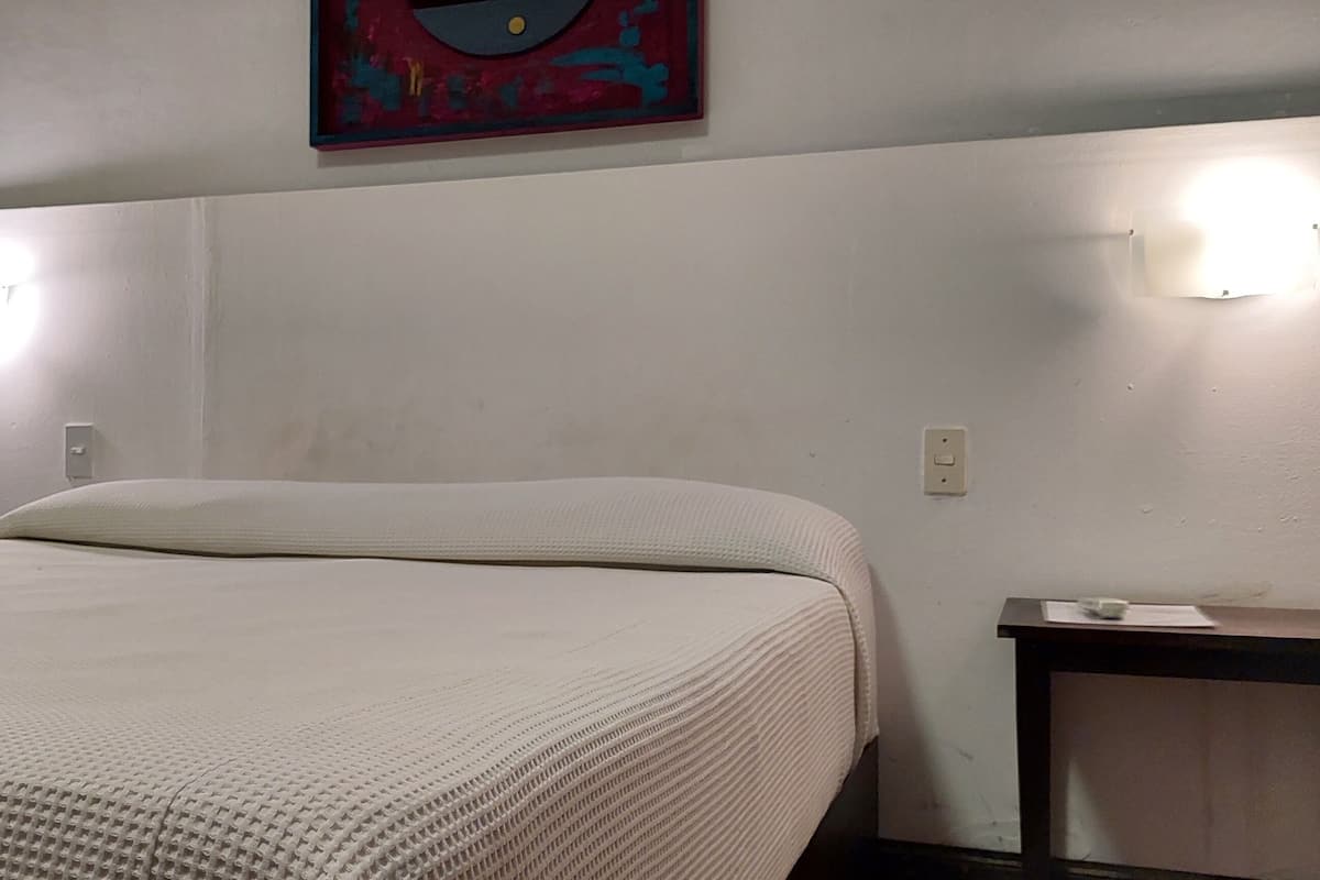 A hotel room with a bed, a nightstand, and a painting on the wall.