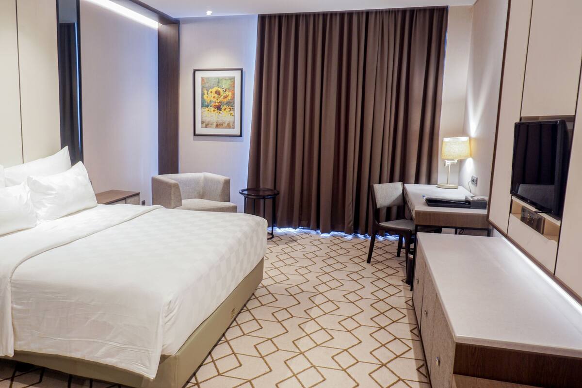 Een hotelkamer met een groot bed, twee stoelen, een bureau met een televisie en een schilderij aan de muur.