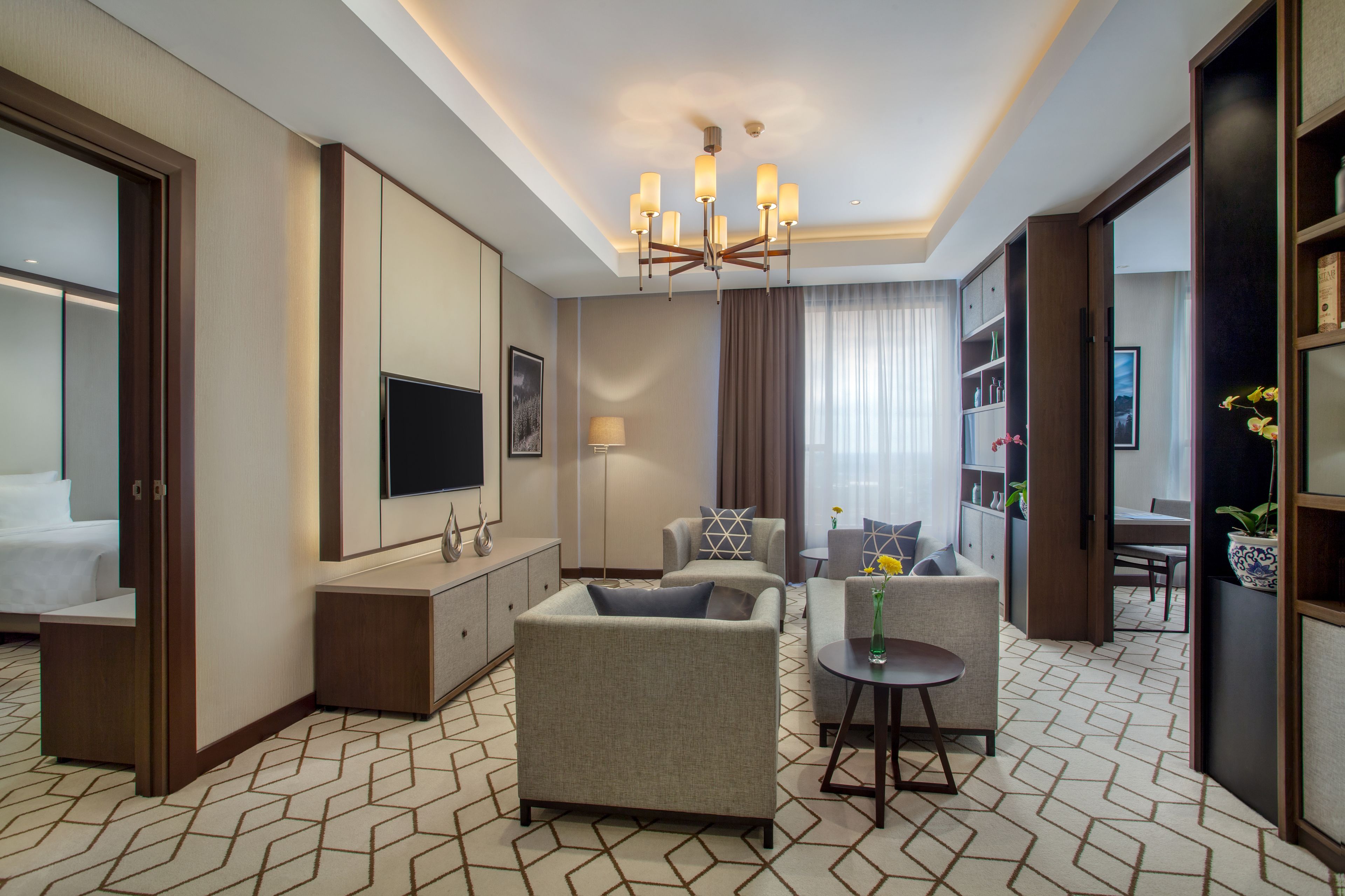 A hotel room with a sofa, armchairs, a TV, a bookshelf, and a dining area.