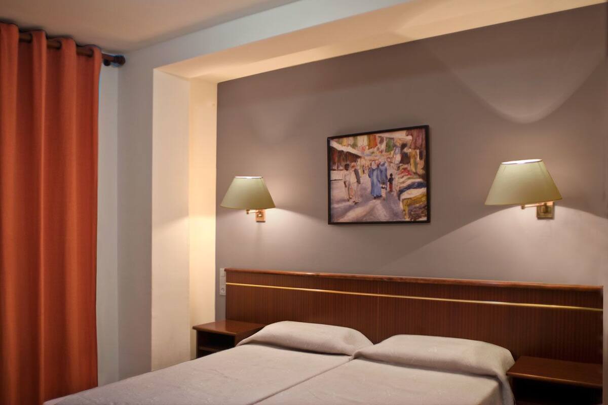 Een hotelkamer met een bed, twee bedlampen, een schilderij aan de muur en een gordijn.