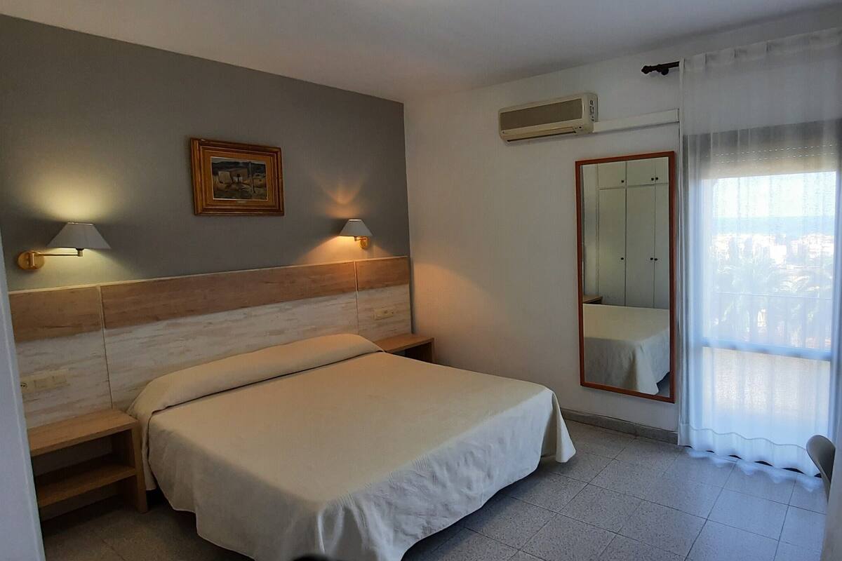 Een hotelkamer met een bed, nachtlampjes, een spiegel en een raam met gordijnen.