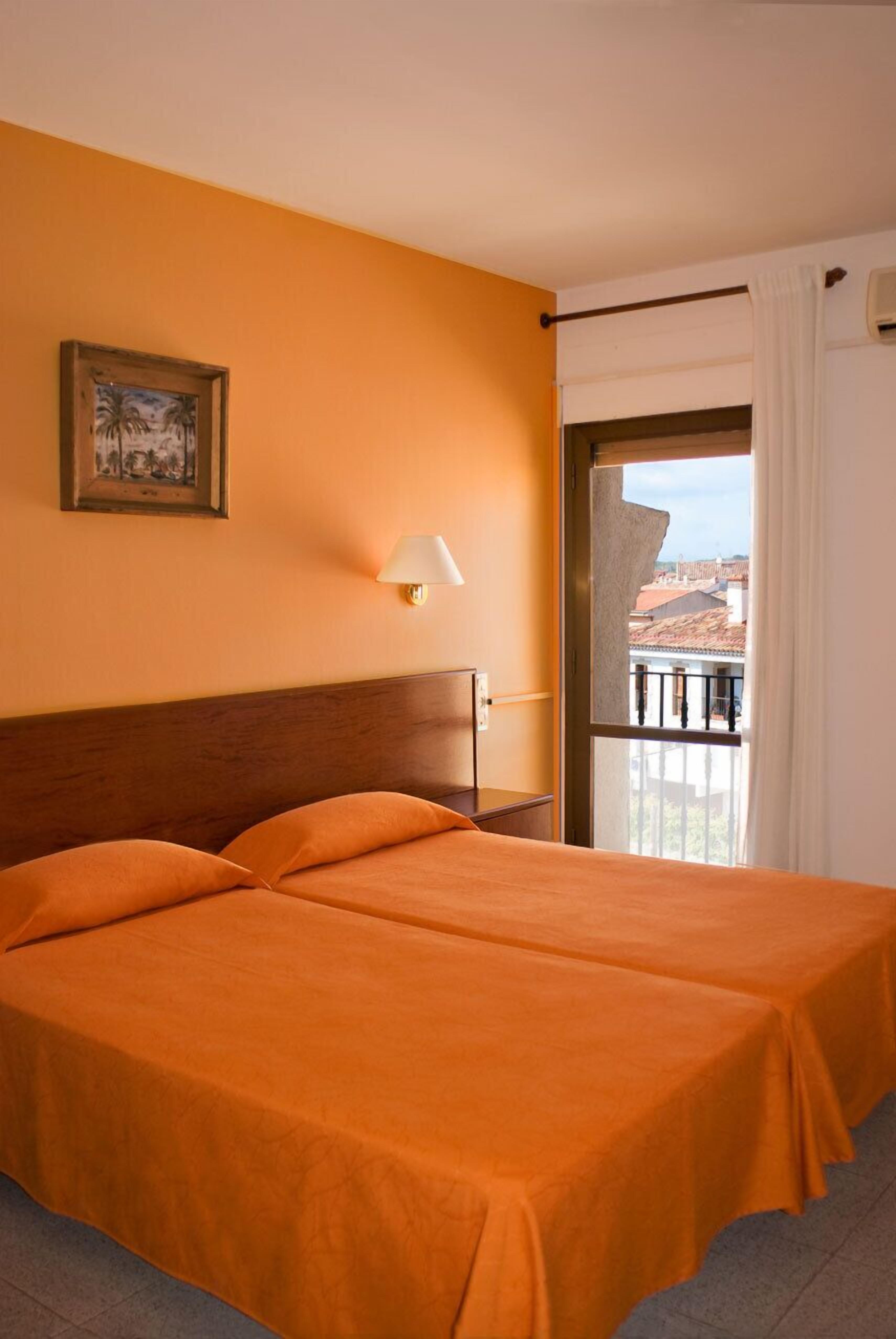 Una habitación con dos camas, un cuadro en la pared, una lámpara y vistas a la ciudad a través de una ventana.