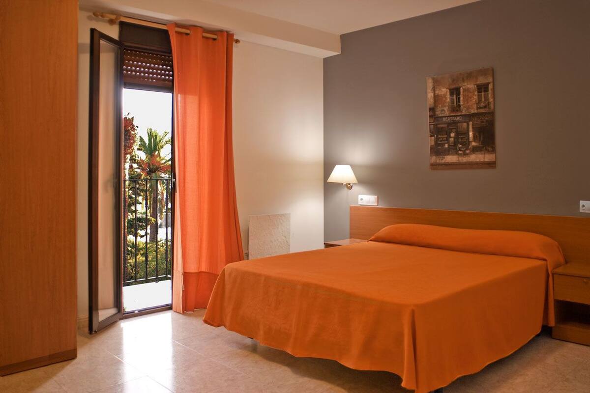 Een hotelkamer met een bed, een nachtkastje, een lamp, een schilderij aan de muur en uitzicht op de omgeving door een schuifdeur.