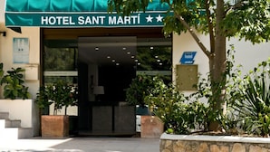 The entrance to Hotel Sant Martí, featuring a green awning, a stone wall, and potted plants. - San Martin (Altafulla)