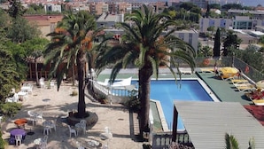A poolside area with palm trees, outdoor seating, and a view of the cityscape. - San Martin (Altafulla)