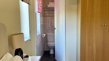 A hotel room with a bed, a nightstand, a lamp, a wardrobe, and a bathroom visible through an open door.