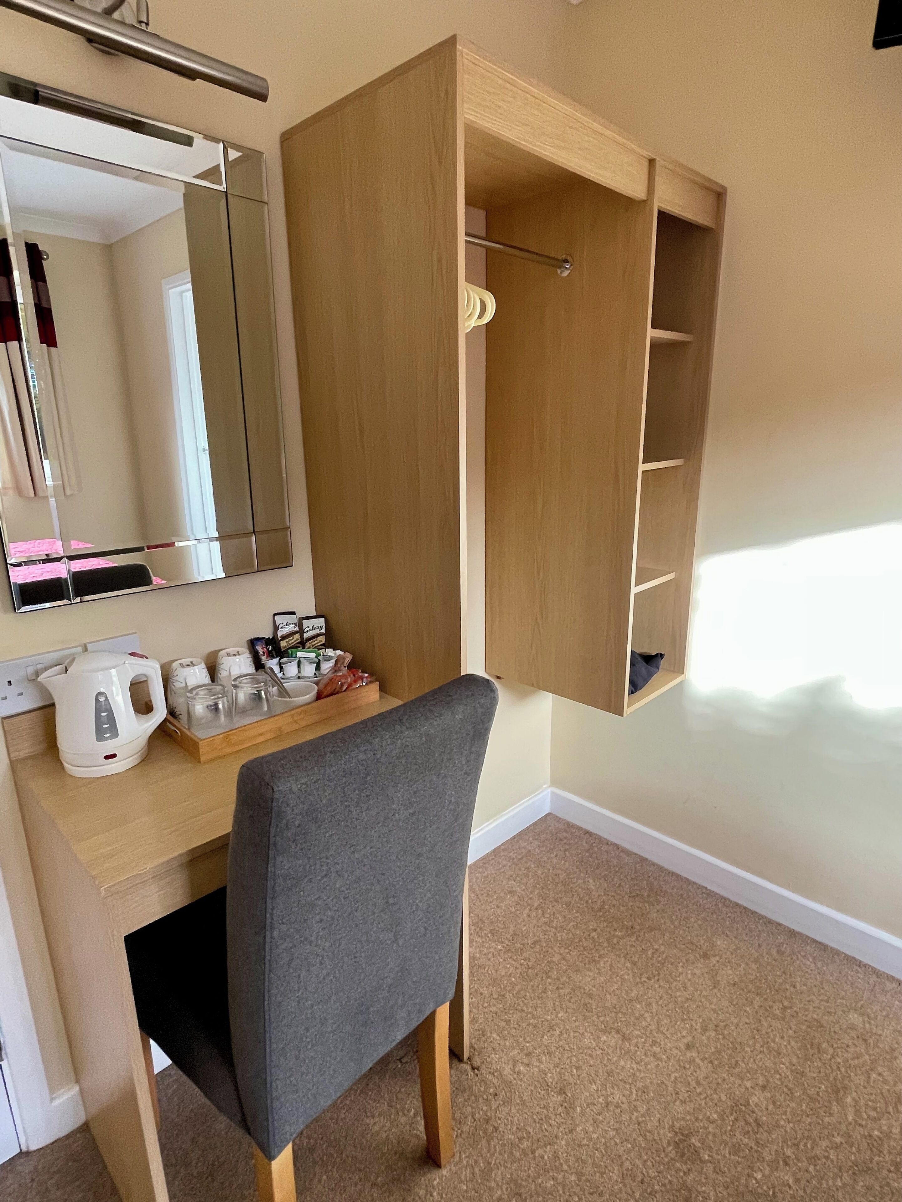 A compact room with a desk, a chair, a mirror, and a wardrobe.