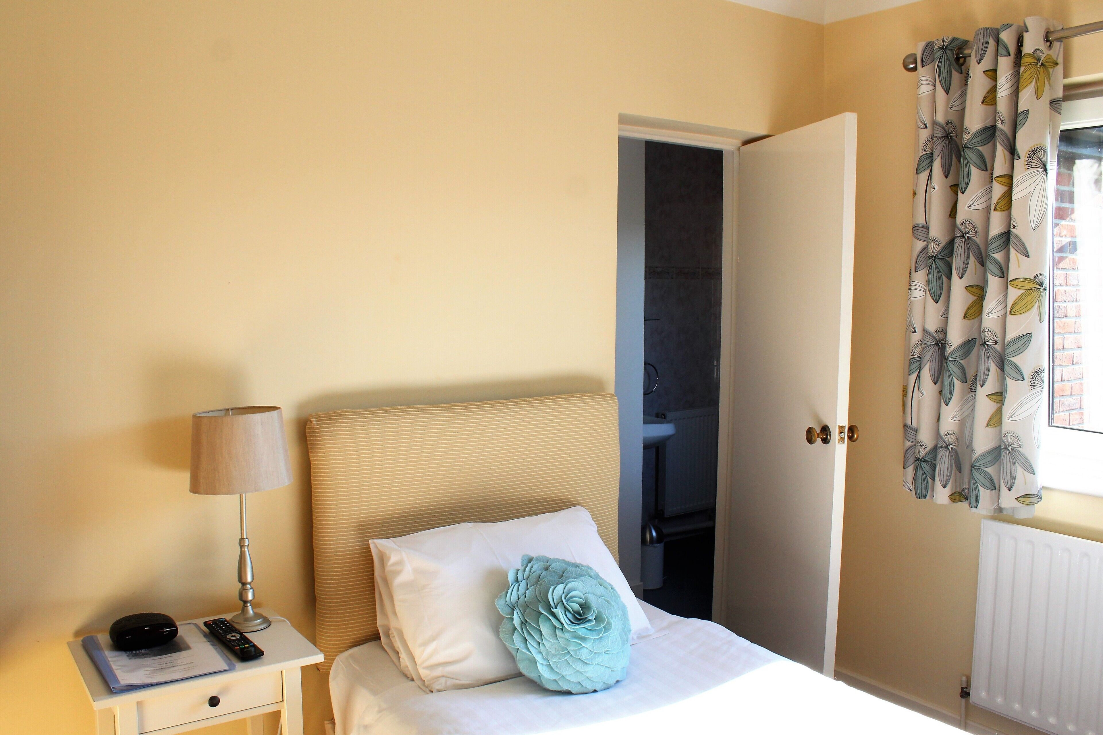 Una camera da letto con un letto, un comodino con una lampada, un telecomando e un cuscino decorativo.