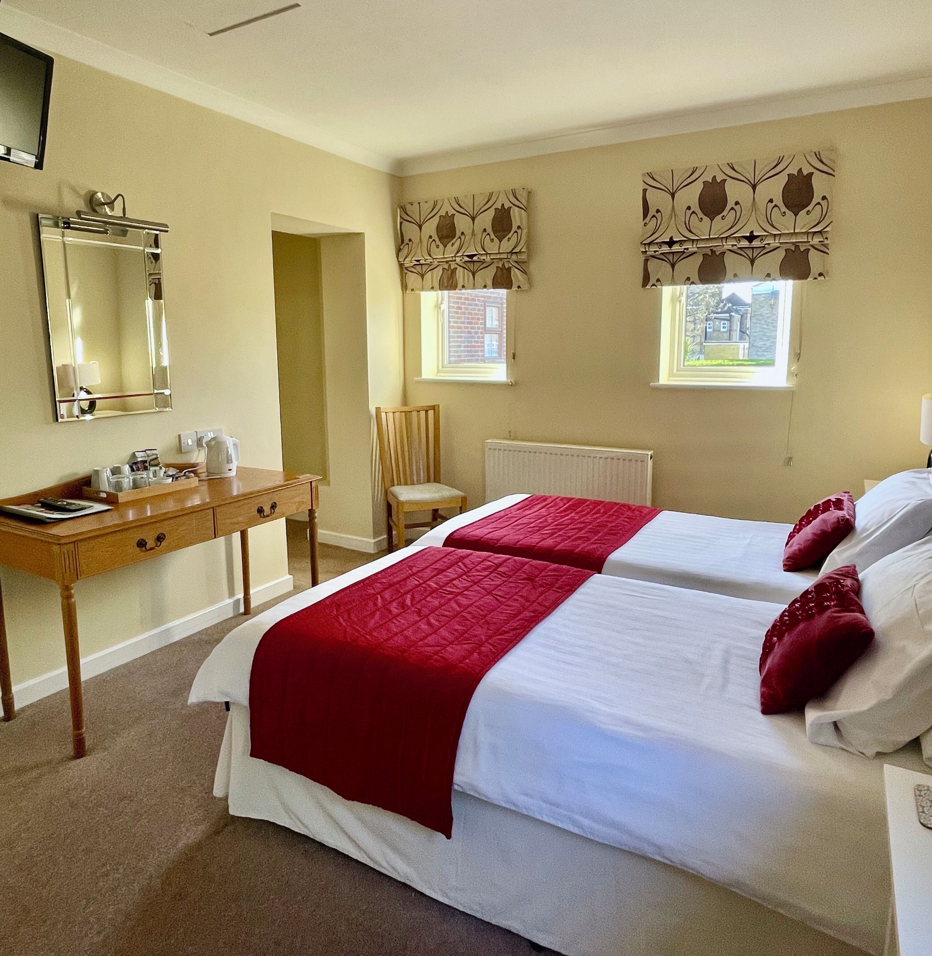 A hotel room with two beds, a desk, a chair, a radiator, and a window with curtains.
