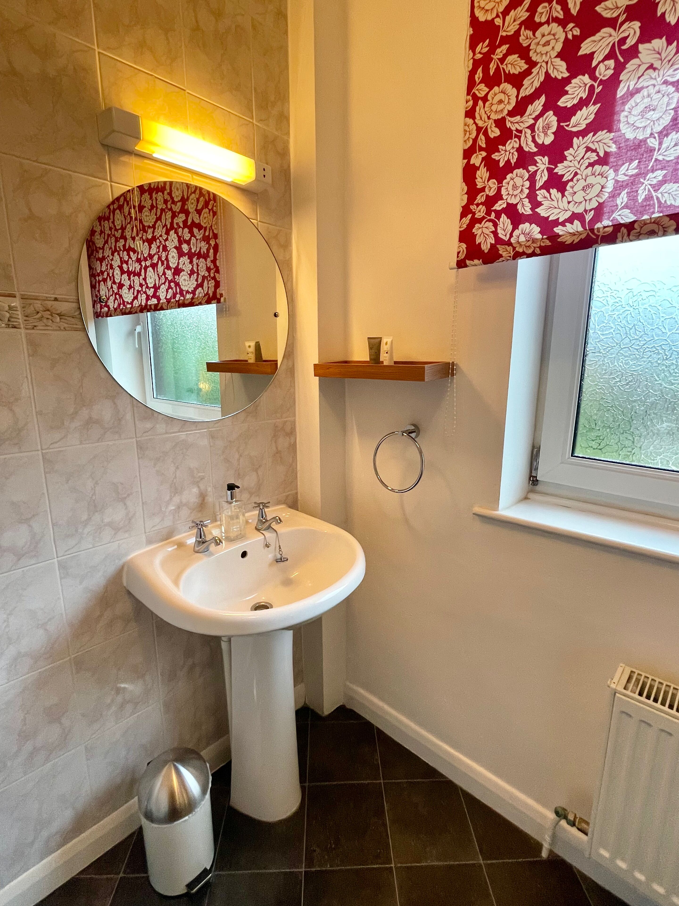 Une salle de bain avec un lavabo sur colonne, un miroir, un porte-serviettes, une fenêtre donnant sur un paysage agréable et un radiateur.