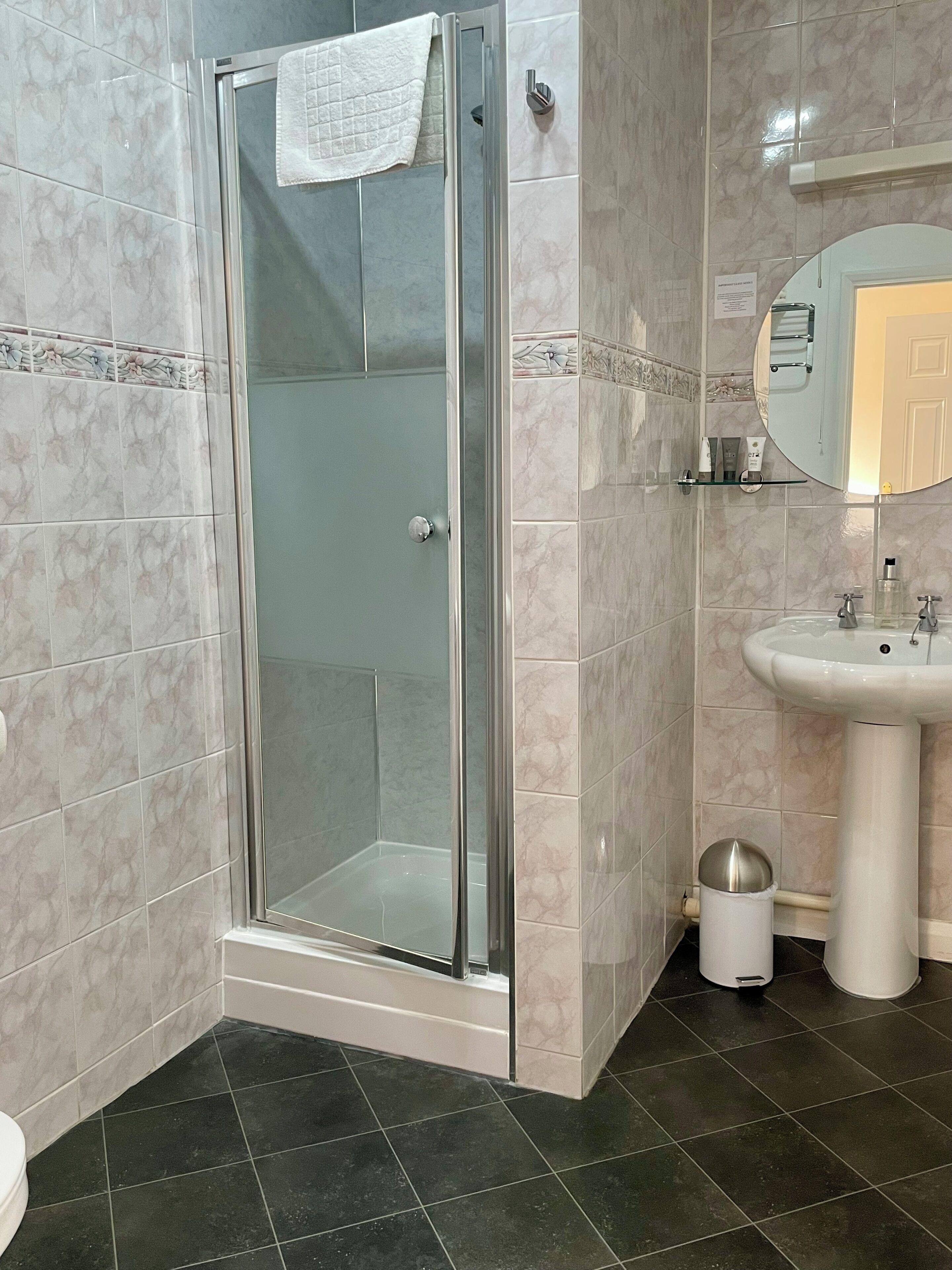 A bathroom with a glass-enclosed shower, a pedestal sink, and a mirror above the sink.