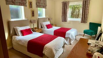 Une chambre d’hôtel avec deux lits, un bureau et une chaise. On y trouve deux tables de chevet avec des lampes, une fenêtre avec des rideaux et une vue sur la verdure à l’extérieur.