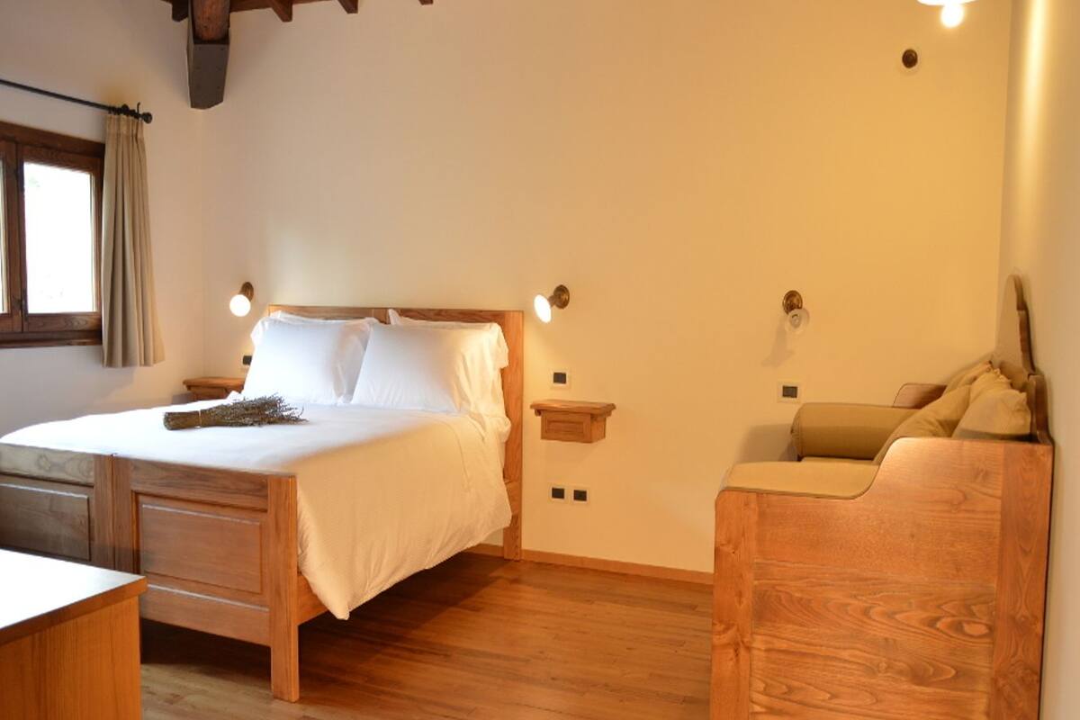 Un dormitorio con una cama de madera, mesitas de noche, un banco de madera y una ventana con cortinas.