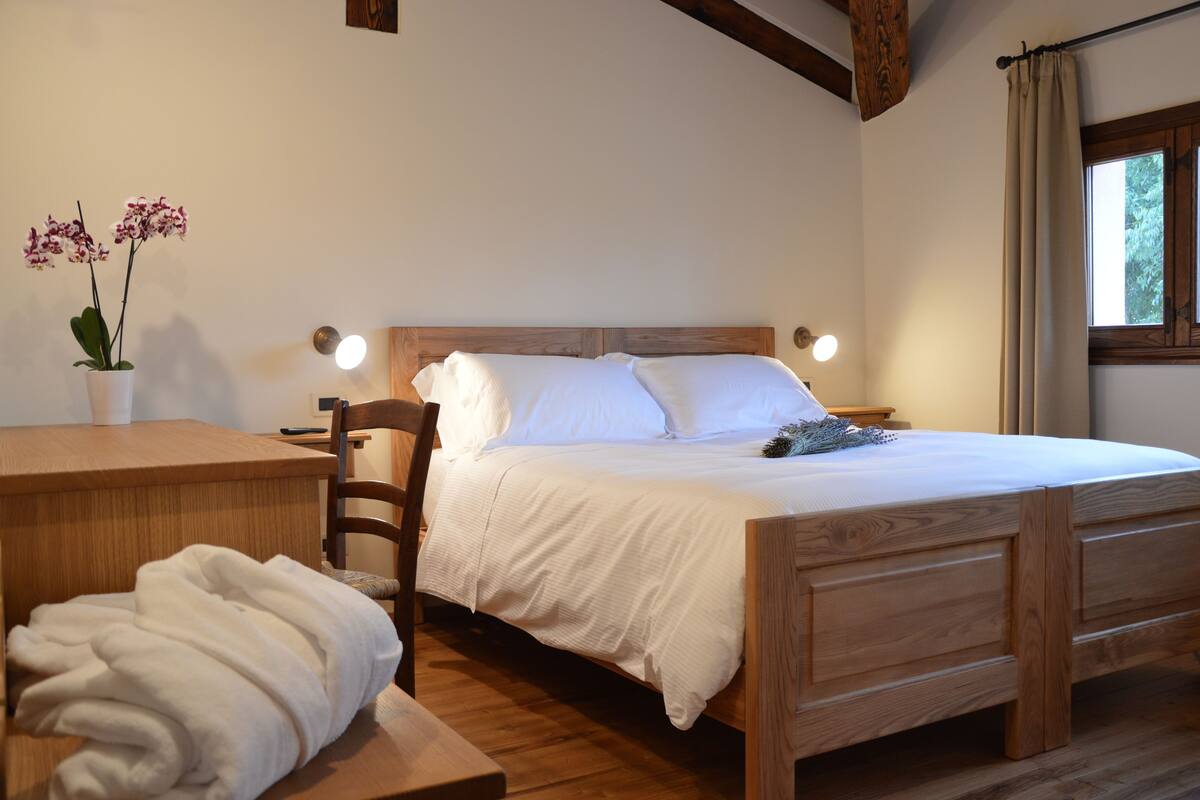 Una cama de madera con ropa de cama blanca, una mesita de noche, una silla y una orquídea en maceta.