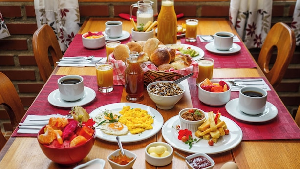 Una mesa de desayuno con diferentes platos, una jarra de jugo y vista a una piscina.