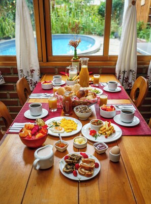 A breakfast table with various dishes, a pitcher of juice, and a view of a swimming pool.