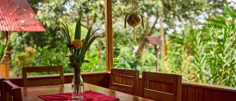 A wooden dining table with a vase of flowers and a red placemat.