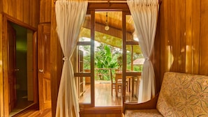 Una habitación de madera con un ventanal grande, cortinas, un banco de madera y vistas a un patio con plantas.