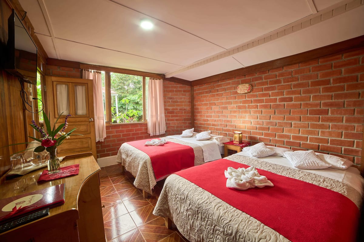 Een hotelkamer met twee bedden, een houten bureau, een spiegel en een bakstenen muur.