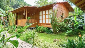 Una cabaña de madera con un porche, rodeada de abundante vegetación y un jardín.