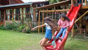 Una estructura de juego de madera con un tobogán rojo en un espacio al aire libre cubierto de césped.