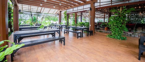An indoor patio area with wooden tables and benches, surrounded by potted plants and a stone wall.