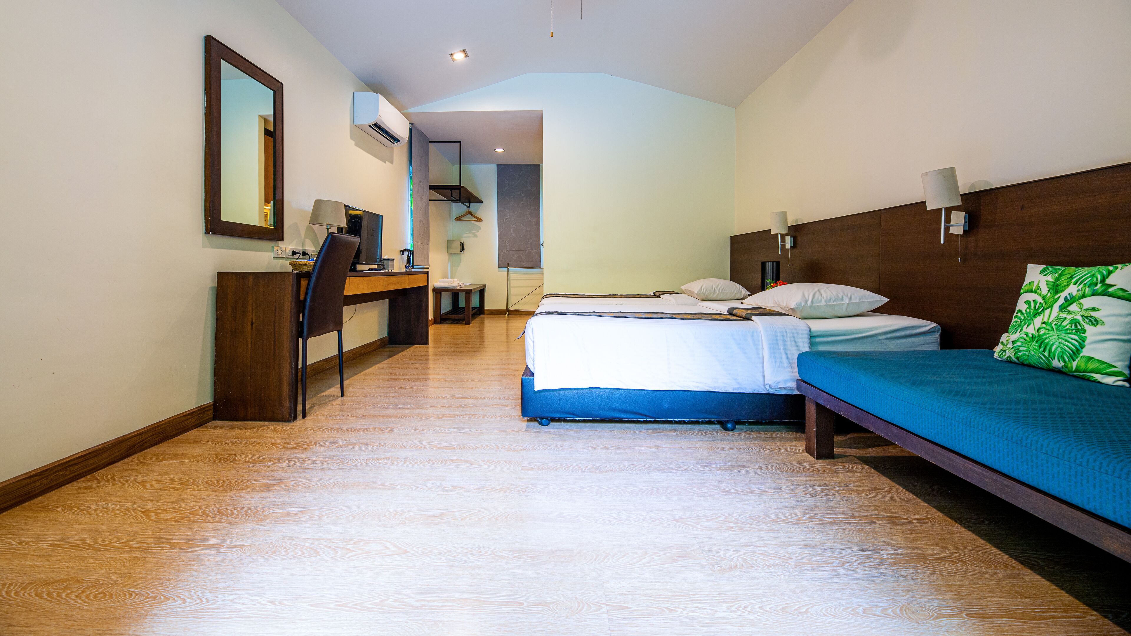 Una habitación de hotel con escritorio, dos camas, un espejo y un equipo de aire acondicionado.