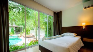 Habitación de hotel con cama, mesita de noche, lámpara y vistas a una piscina y zonas verdes exteriores.