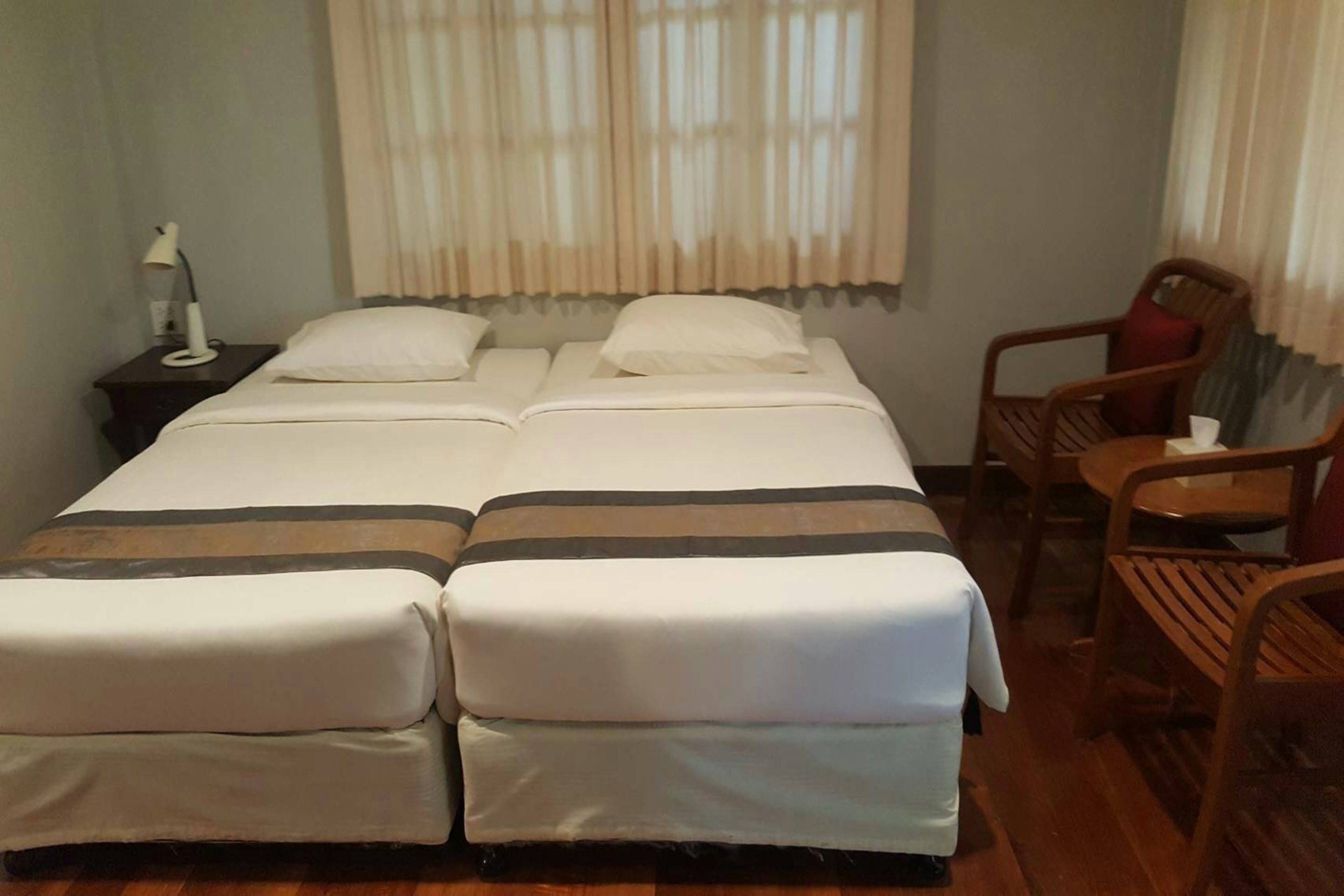 Habitación de hotel con una cama grande, una mesita de noche con lámpara y dos sillas de madera.