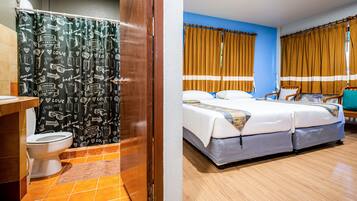 A bathroom with a shower curtain featuring bathroom-related illustrations and a bed with a striped curtain in a room with blue walls.