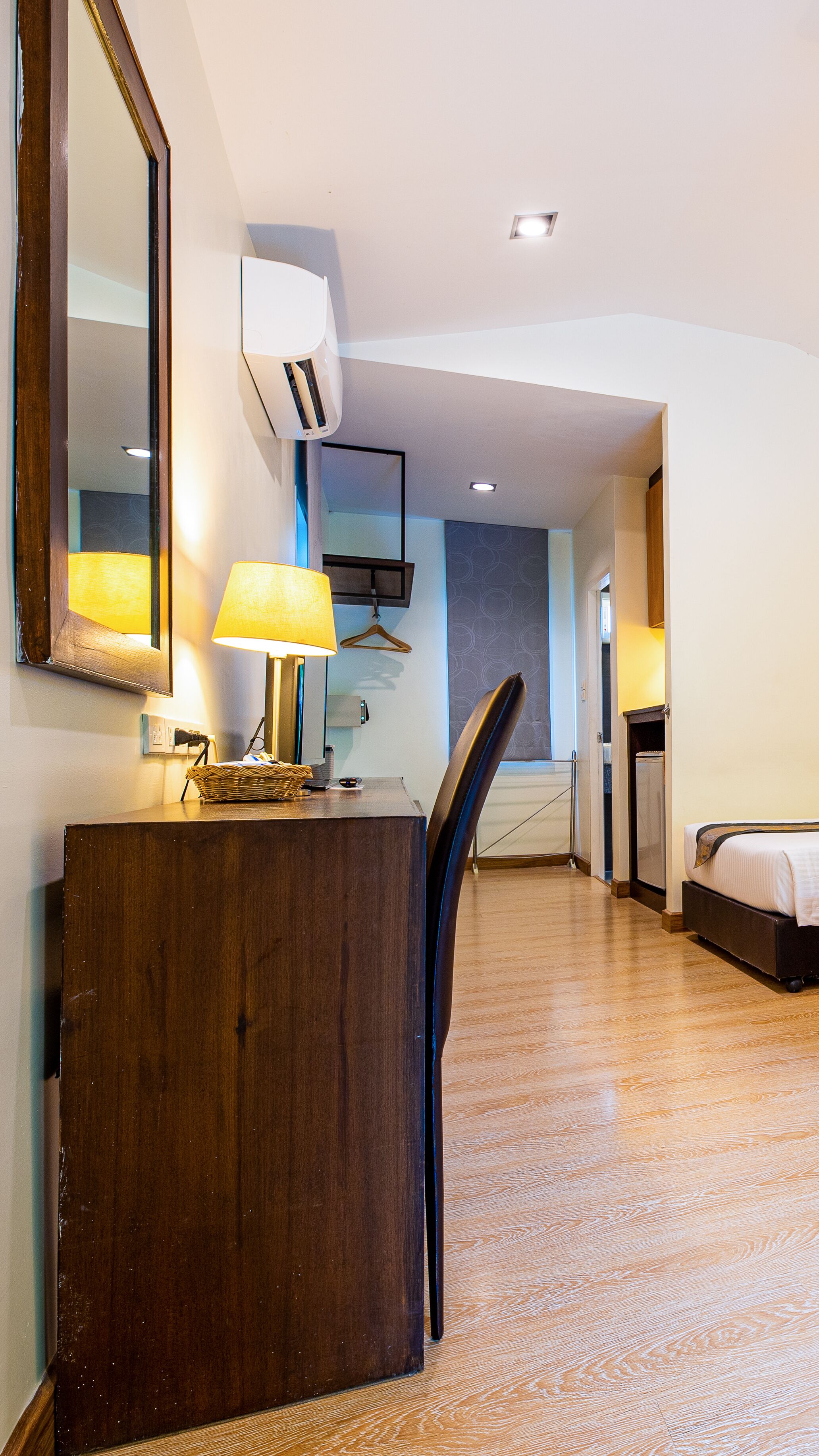 A hotel room with a wooden desk, a chair, a bed, a mirror, and a hanging light fixture.