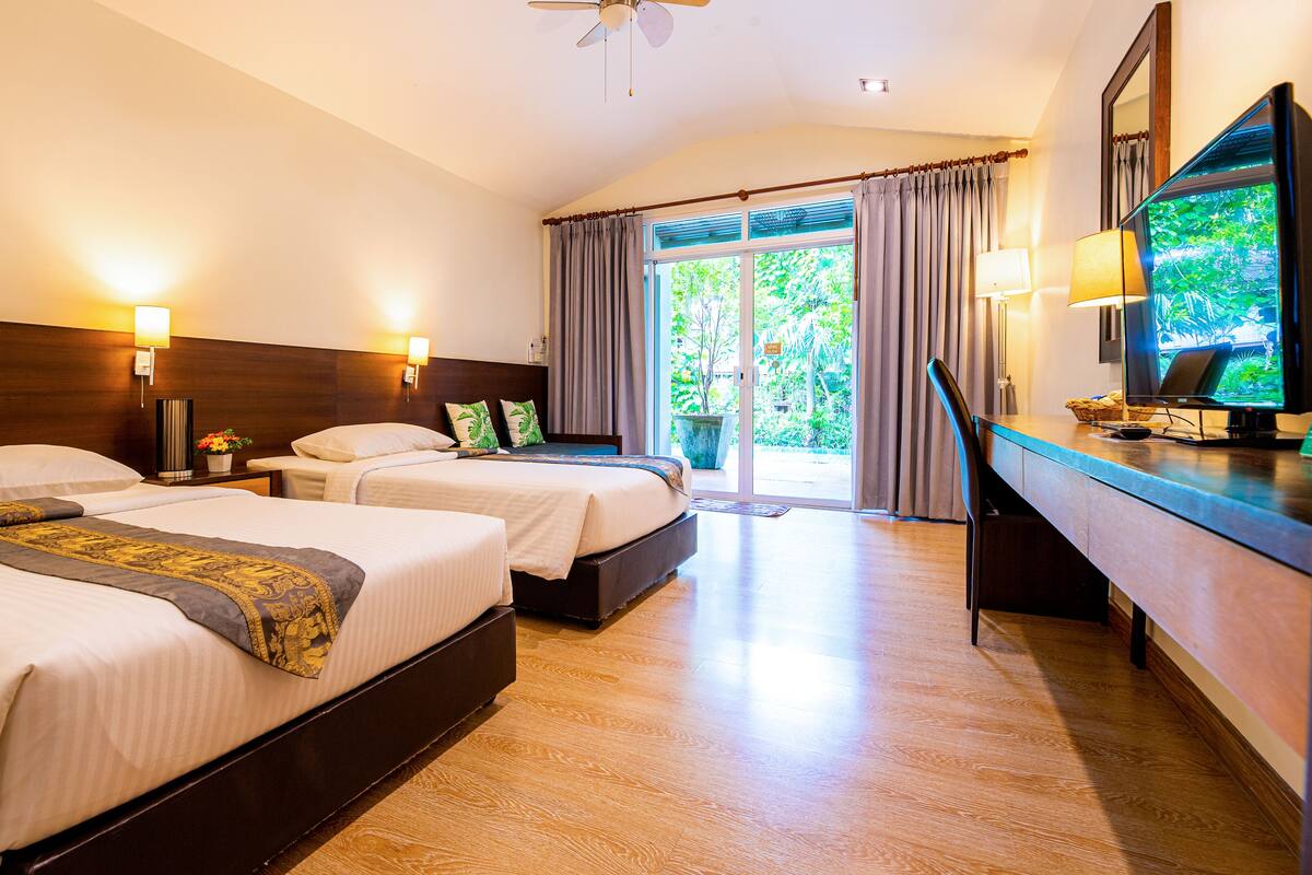 A hotel room with two beds, a desk, a chair, a television, and a view of the outdoors.