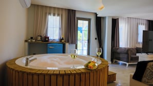 A room with a wooden bathtub, a glass of white wine, a sofa, and a television.