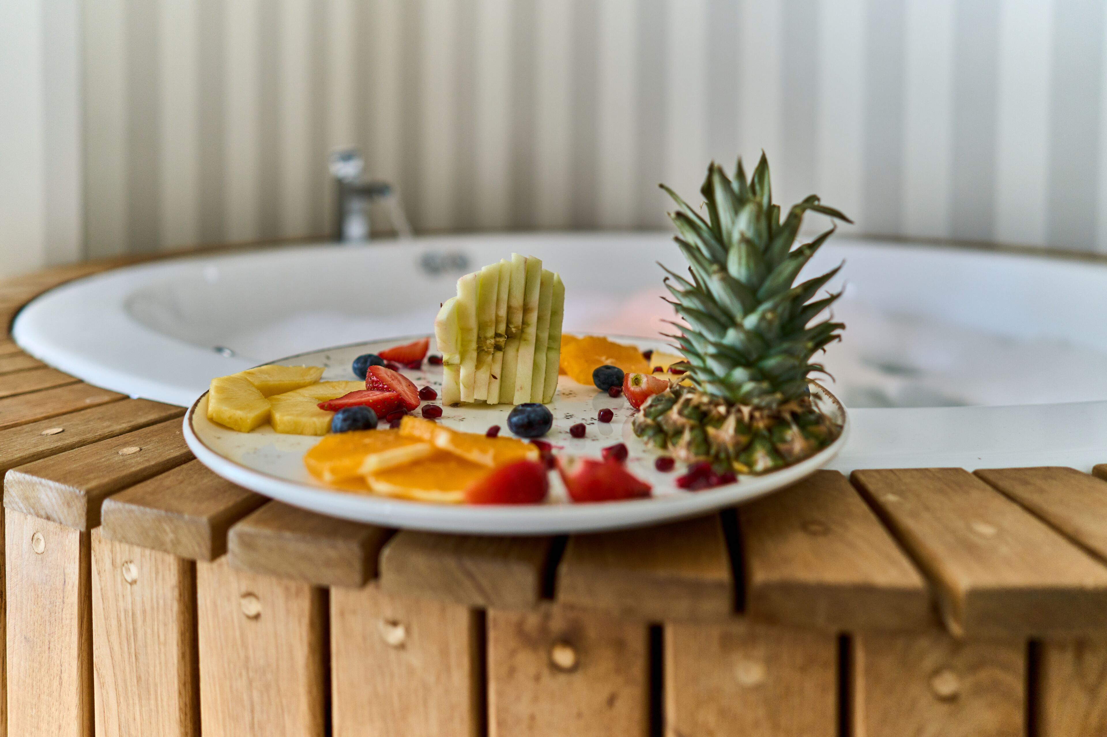Une table en bois sur laquelle se trouve une assiette de fruits, notamment de l’ananas, des bananes, des fraises, des myrtilles et des tranches d’orange.